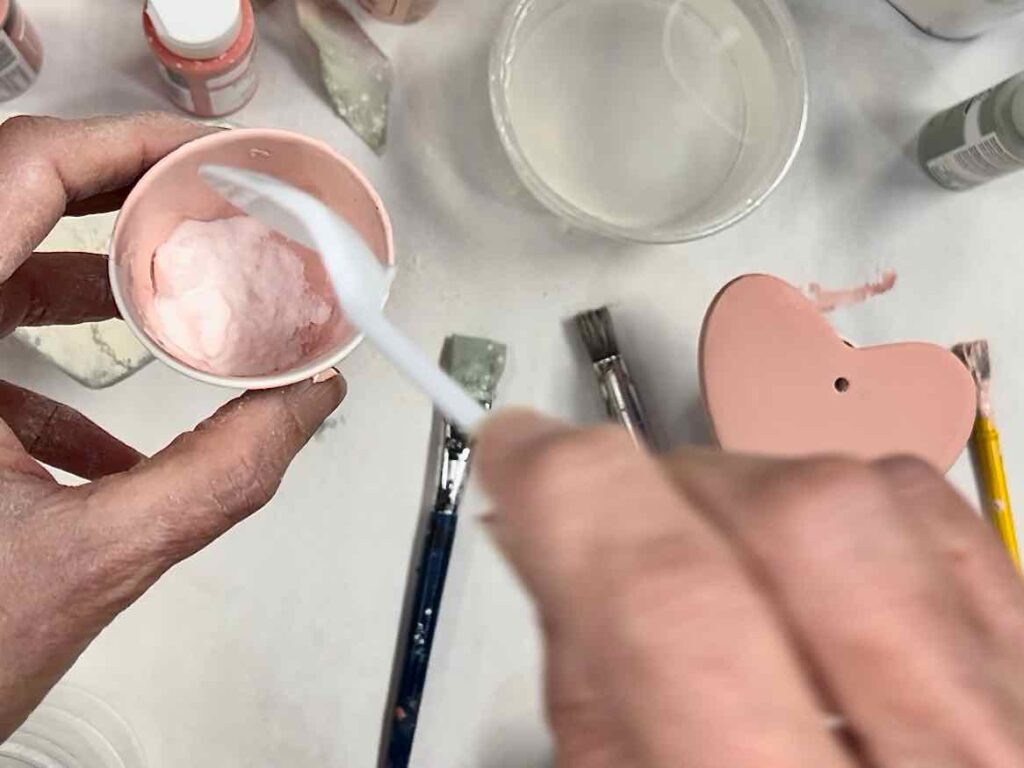 closeup of a large spoonful of baking soda being added to a small cup with paint in it