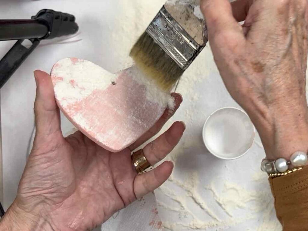 Woman brushing the excess flour off of the heart once the paint is dry