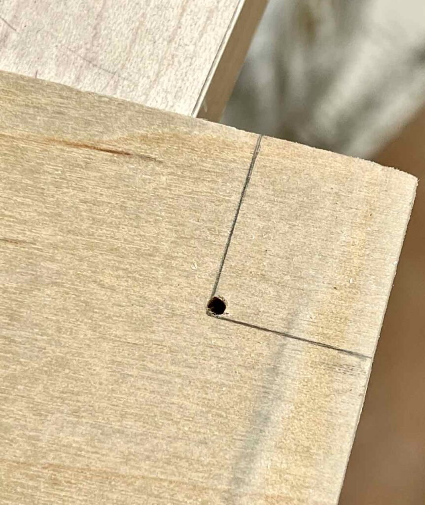 closeup of a notch drawn on the corner of a shelf with a hole drilled just inside the corner.