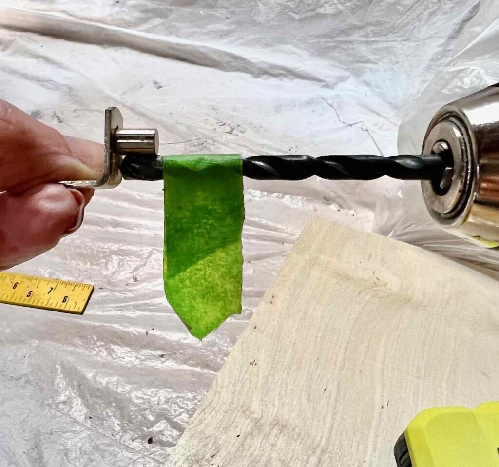 ckoseup of a woman's fingers holding a shelf peg next to a drill bit with painters tape