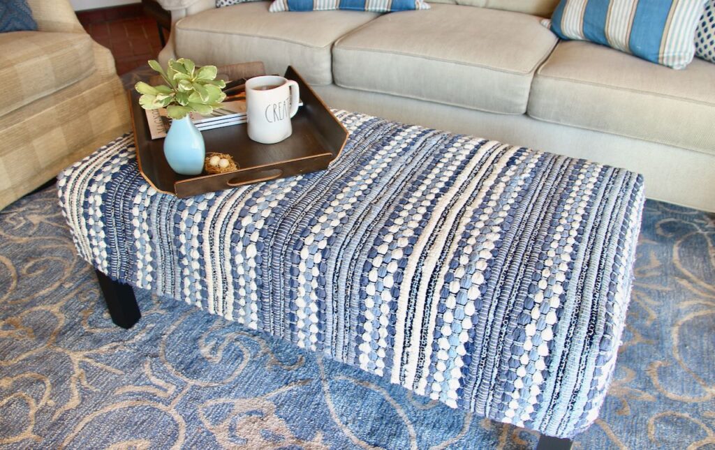 Ottoman slipcovered with a blue and white rag rug with a tray holding a mug, small vase and magazine on top