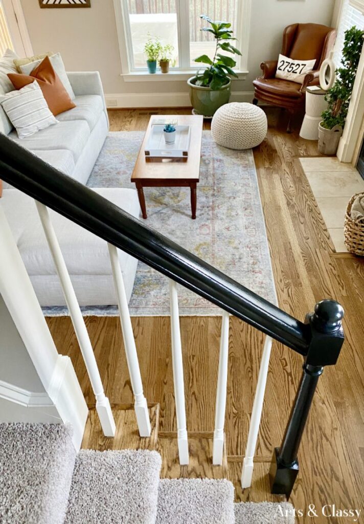 closeup of a handrail painted black over white balusters with a living room in the distance