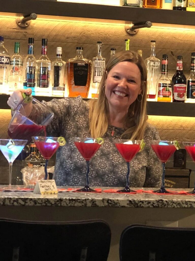 A woman behind the bar pouring cocktails into martini glasses