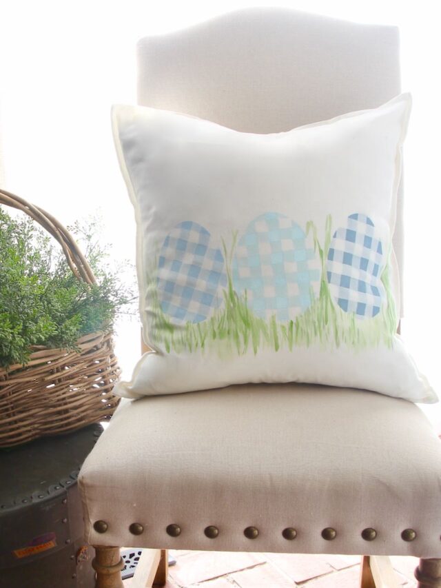Buffalo Plaid Eggs painted pillow shown on a linen chair next to a bakset of greenery