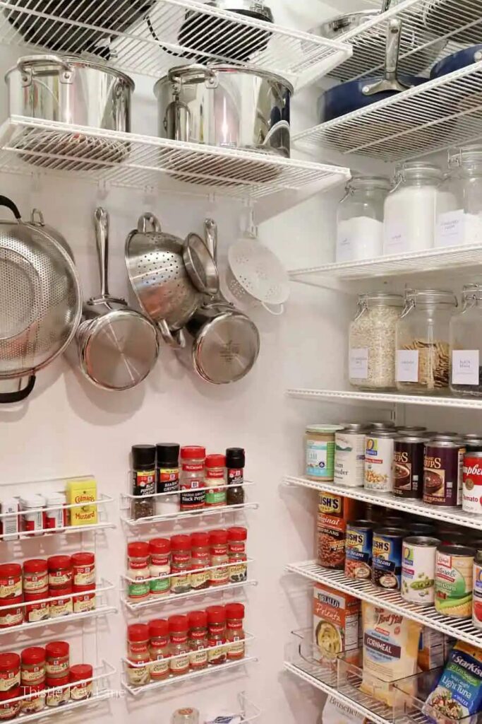 The inside of a small pantry with loads of wire shelves holding all the post and pans as well as food containers
