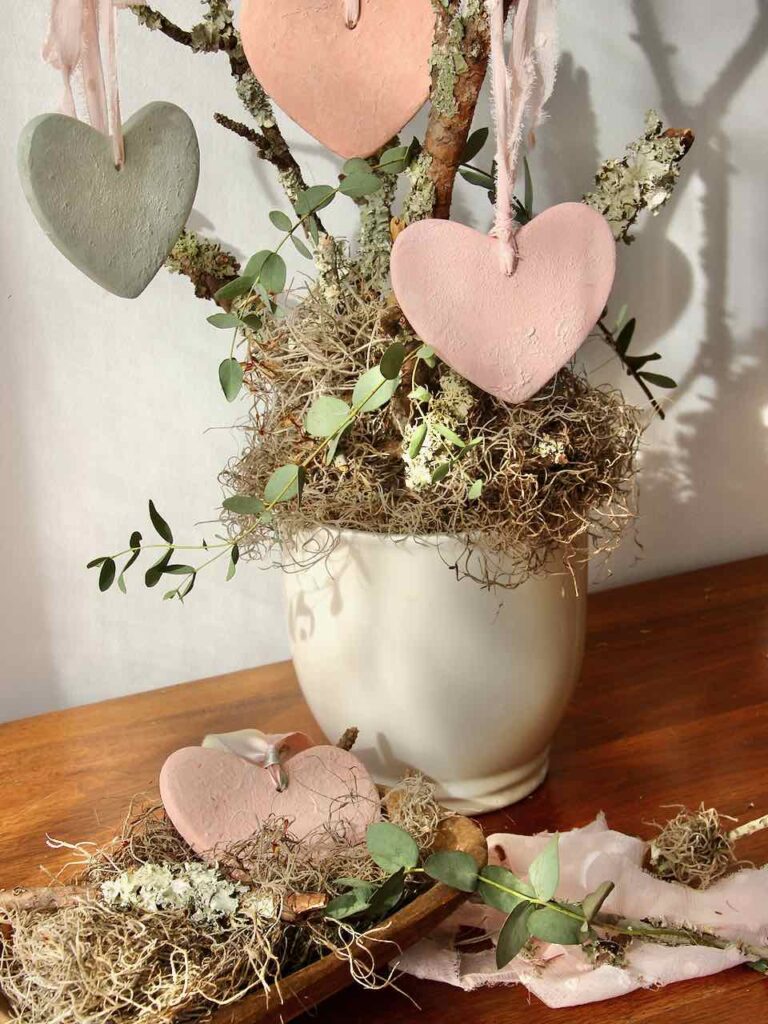 3 finished hearts hanging from branches above one heart propped in a dough bowl,