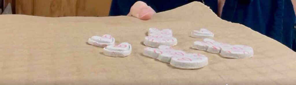 air dry clay pieces that have been silk screened and cut are on parchment paper on a cooling rack as they cure