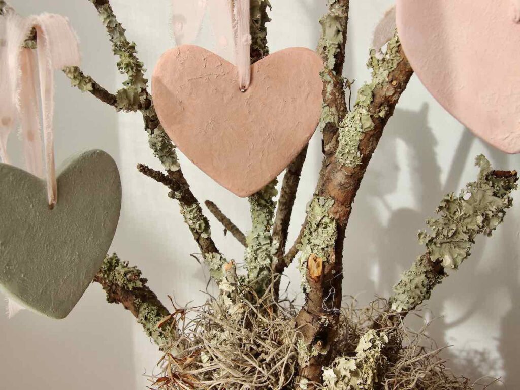 closeup of three finished clay hearts hanging from branches with lichen and moss