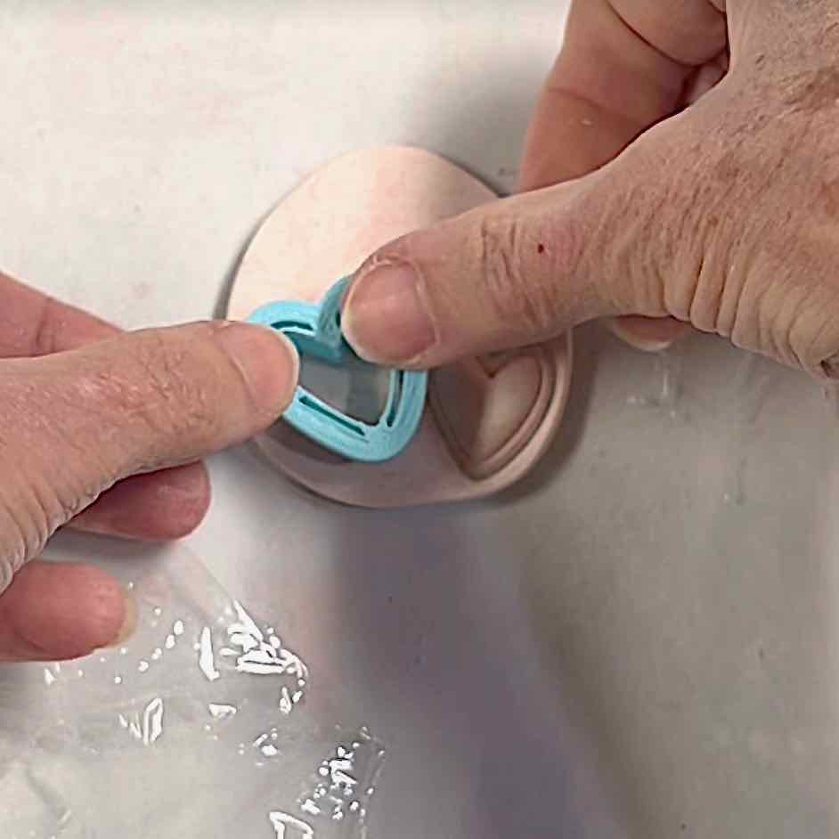 fingers pressing a small heart shaped cutter into clay without plastic wrap