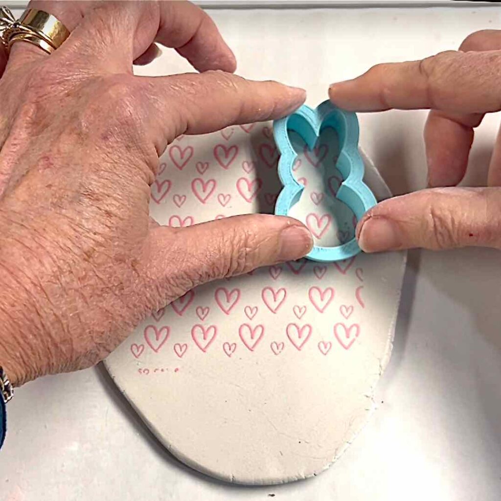 fingertips pressing a bunny cutter into a screen-printed sheet of clay