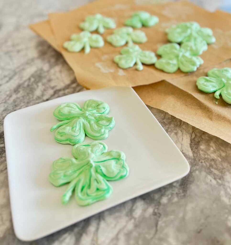 two cookies are on a serving plate with more cookies on the parchment paper covered cookie sheets