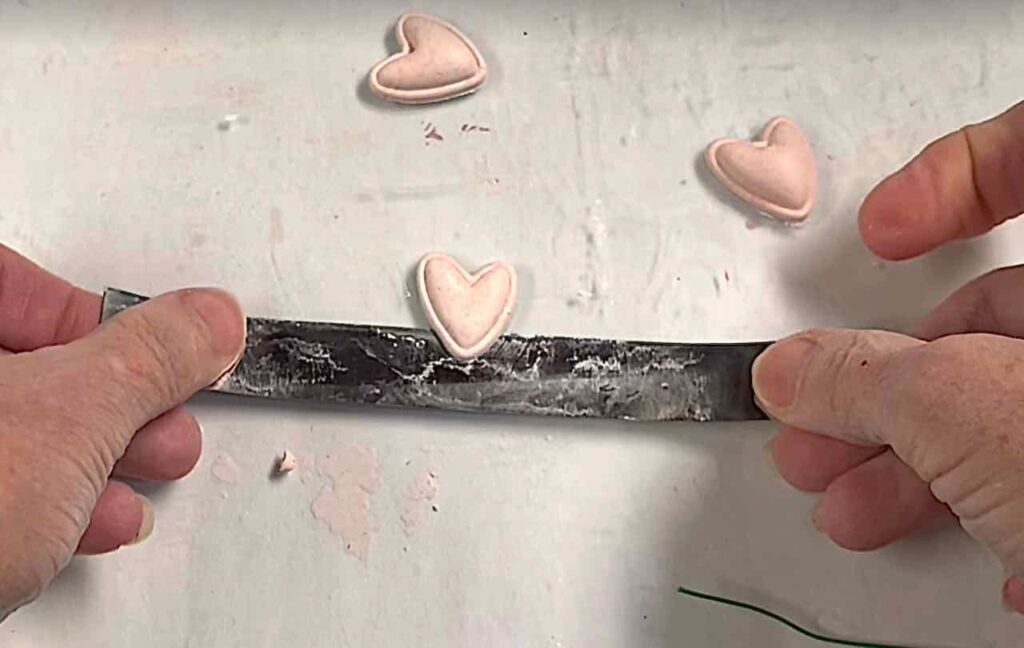 fingertips holding a tissue blade to lift a small clay heart from the work surface