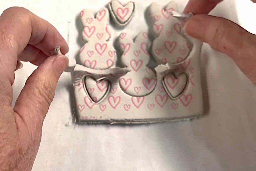 fingers pulling away the background scrap clay from around cut bunnies and hearts