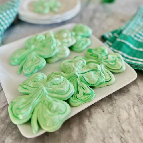 six large shamrock cookies are on a serving plate on a granite counter