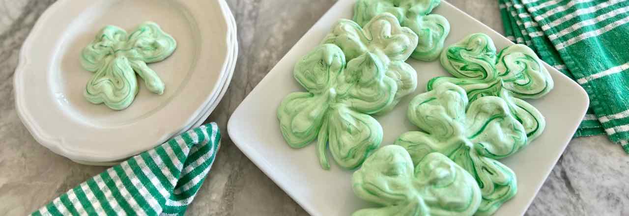 wide closeup shamrock meringue cookies on a plate with check napkins next to them