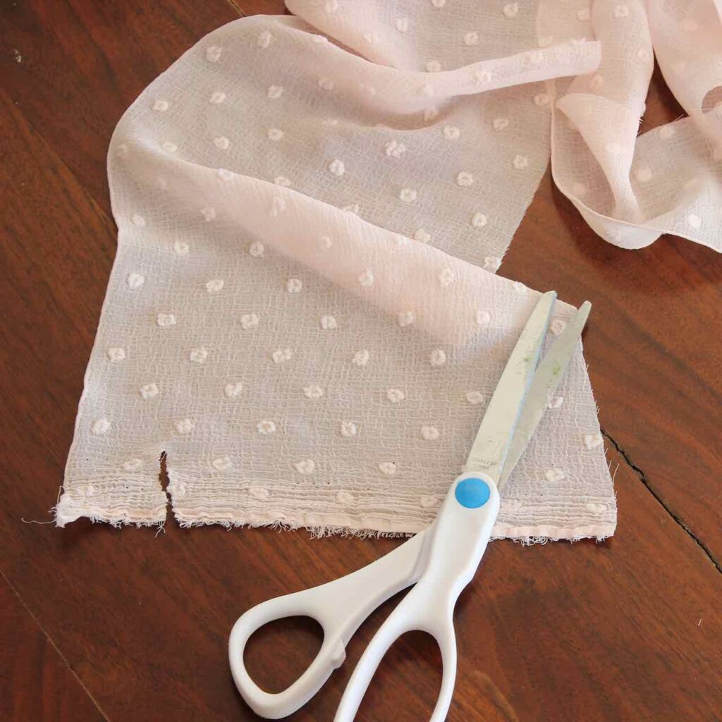 Scissors laying on a piece of chiffon fabric with a small cut in the edge of the fabric