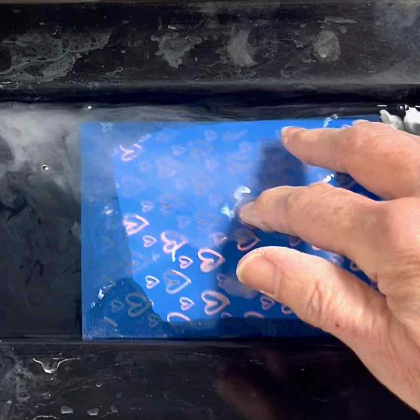 hand swishing paint-covered screen in water
