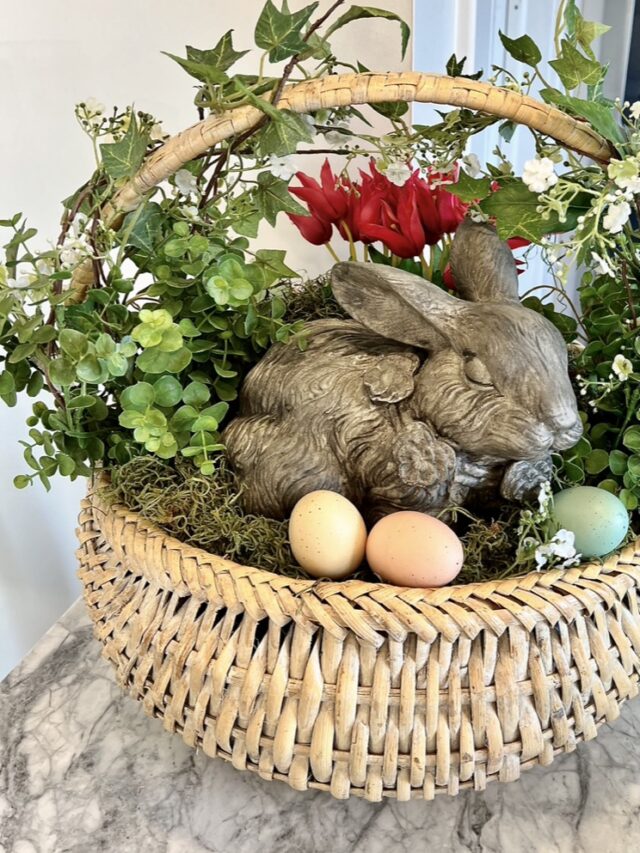 Faux concrete garden statue bunny is in a large basket with a few Easter eggs and plants