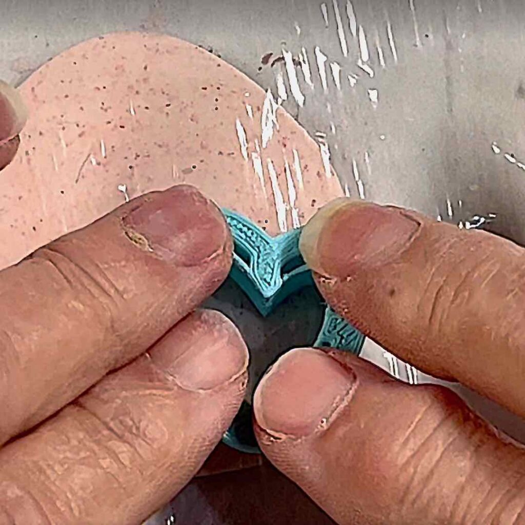 fingerttips pressing a small heart cutter into clay covered with kitchen plastic wrap