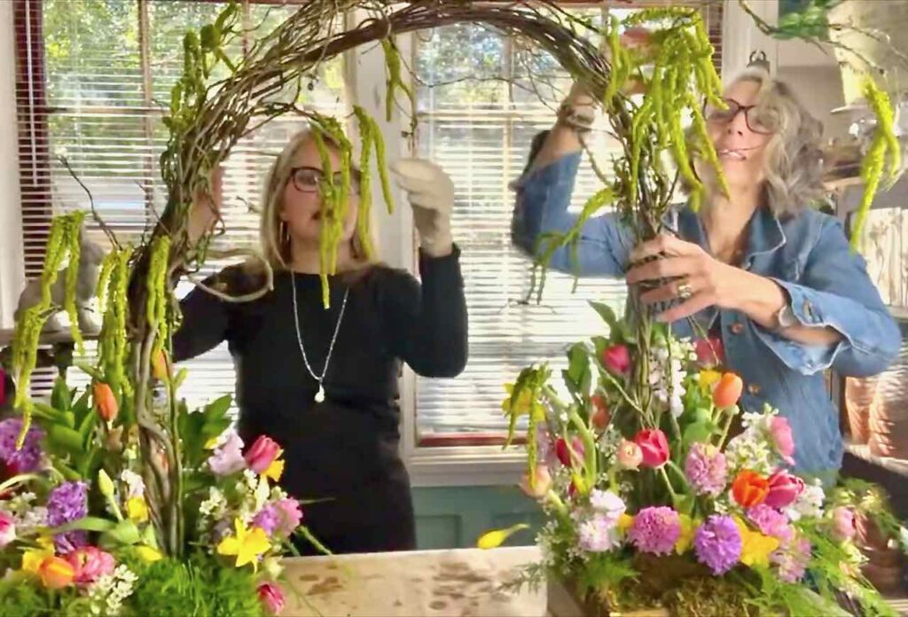 Two women adding drapey Amaranthus to the willow arbor