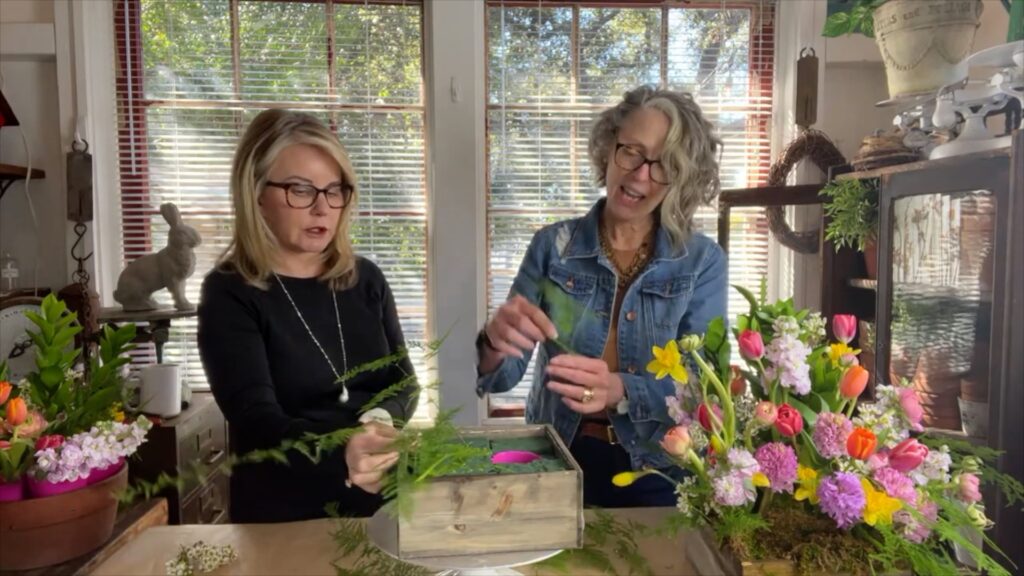 Two women adding fresh floral greens to an Easter floral arrangement