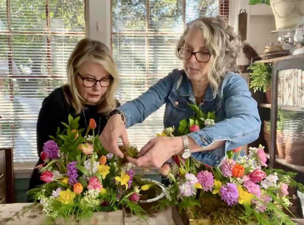 two women adding dried moss under the flowers in the arrangement