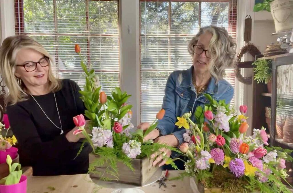 Two women adding tulips and other Spring flowers to a floral arrangement