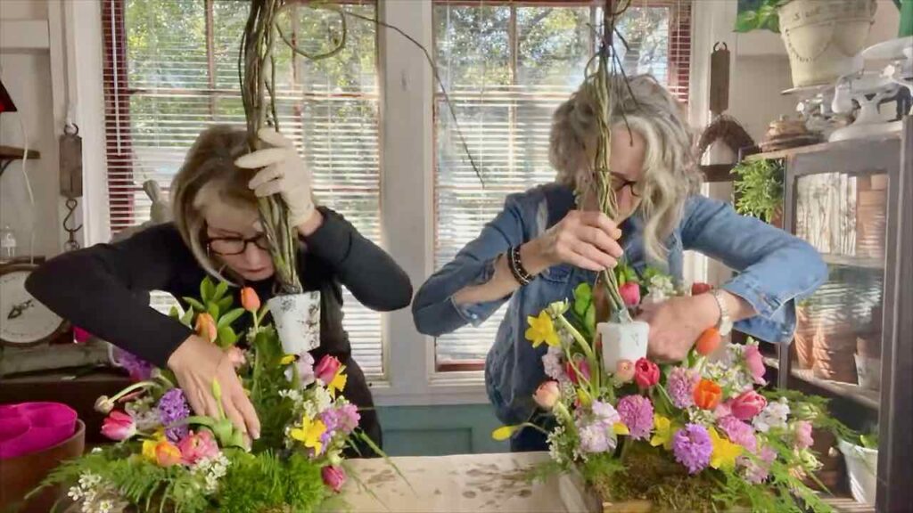 Two women each adding an end of a willow arbor to a flower arrangement on either side