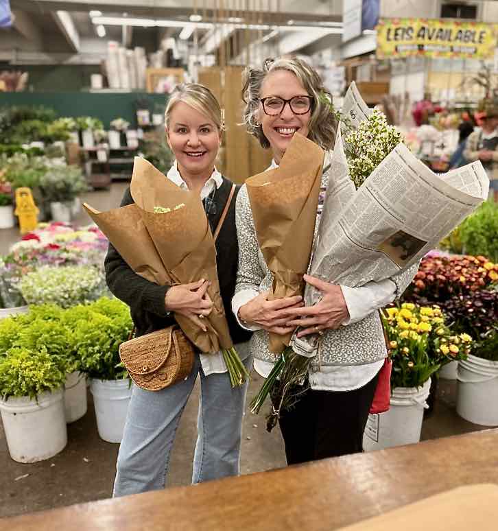 arms full of bundles of Spring flowers are held by two smiling women