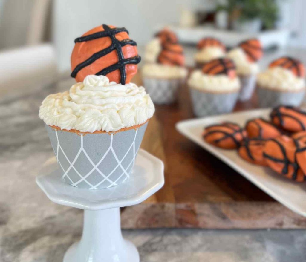 closeup of a basketball cupcake on a pedestal with and cookies in the background