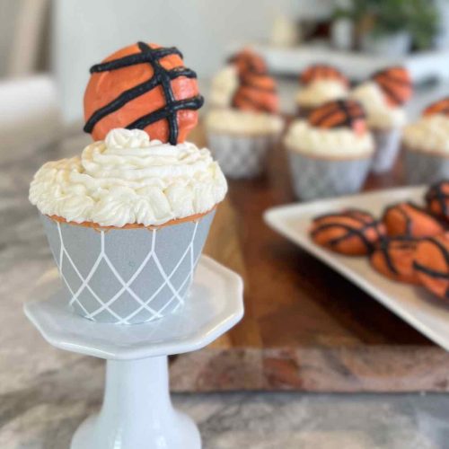 closeup of a basketball cupcake on a pedestal with and cookies in the background