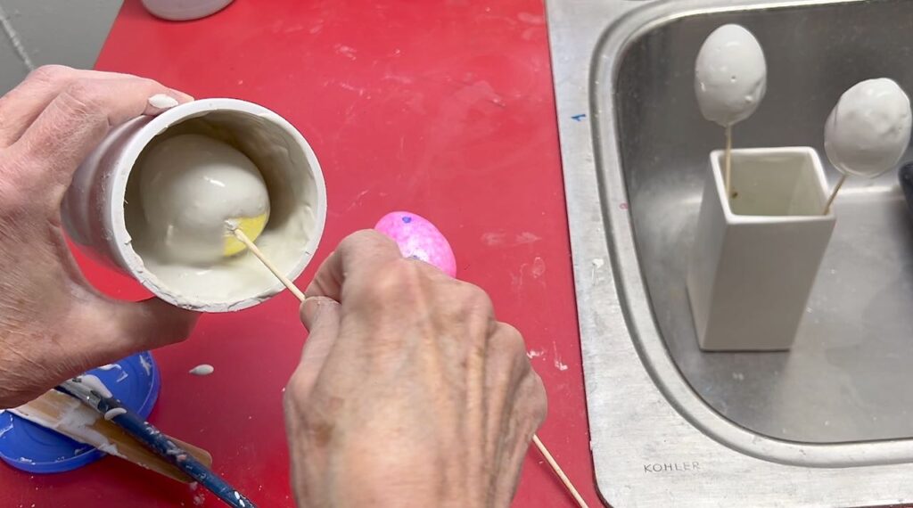 a foam egg on a skewer is being dipped in the container of slurry