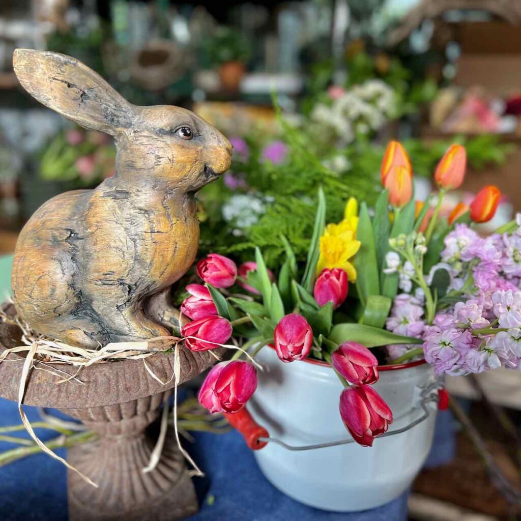 A bunn statue is on vintage garden urn next to a bucket of fresh cut Spring flowers