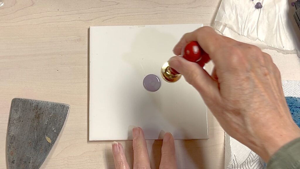 a puddle of melted wax is on a smooth tile and a hand is holding the wax stamp over it