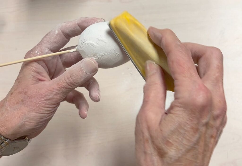 one hand is holding an egg while the other hand sands it using the micro sander