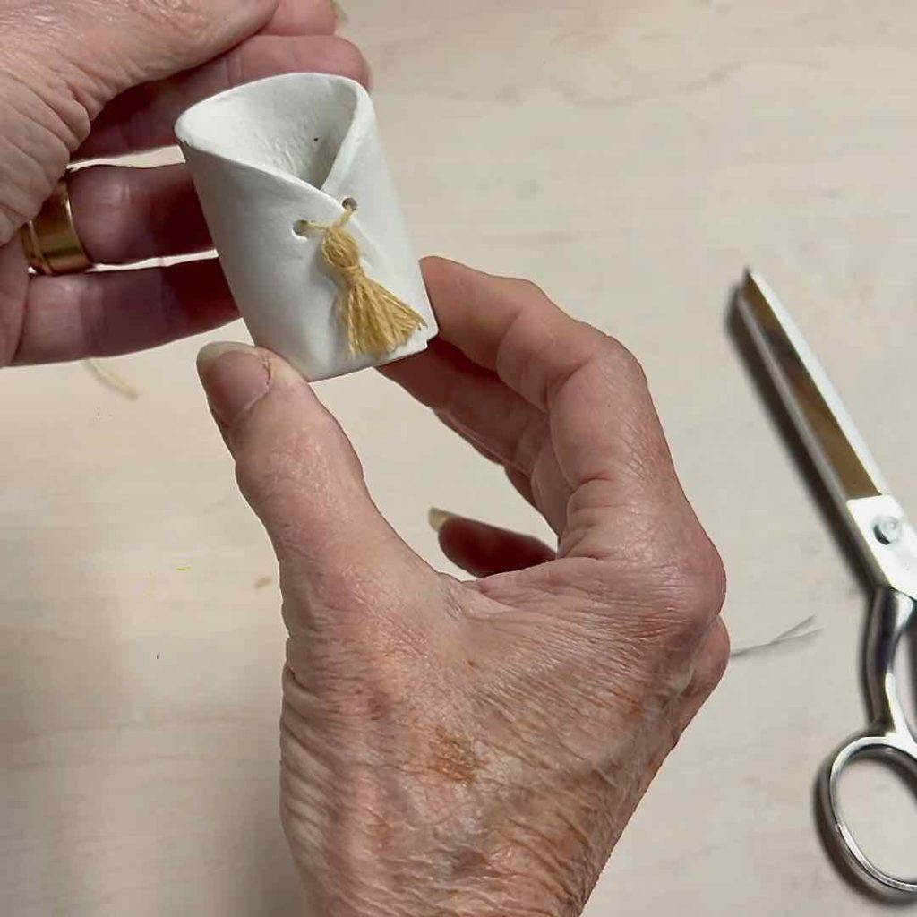 closeup of hands holding finished pot with a tiny tassel added