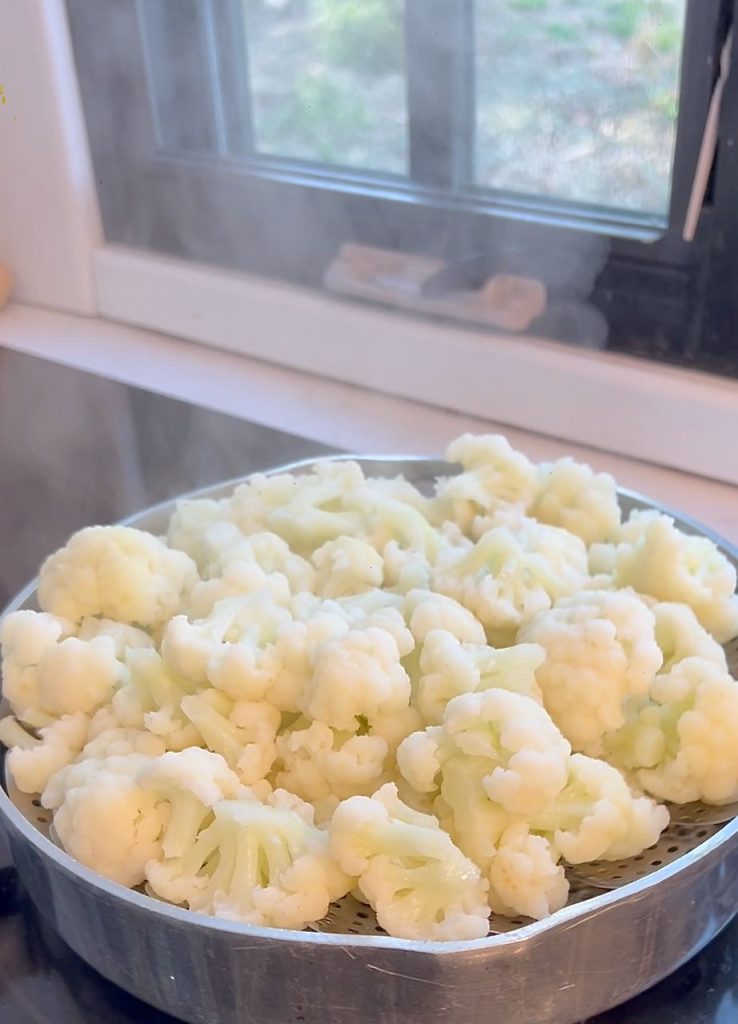 Closeup of steam rising from cauliflower florets in a steamer on the cooktop