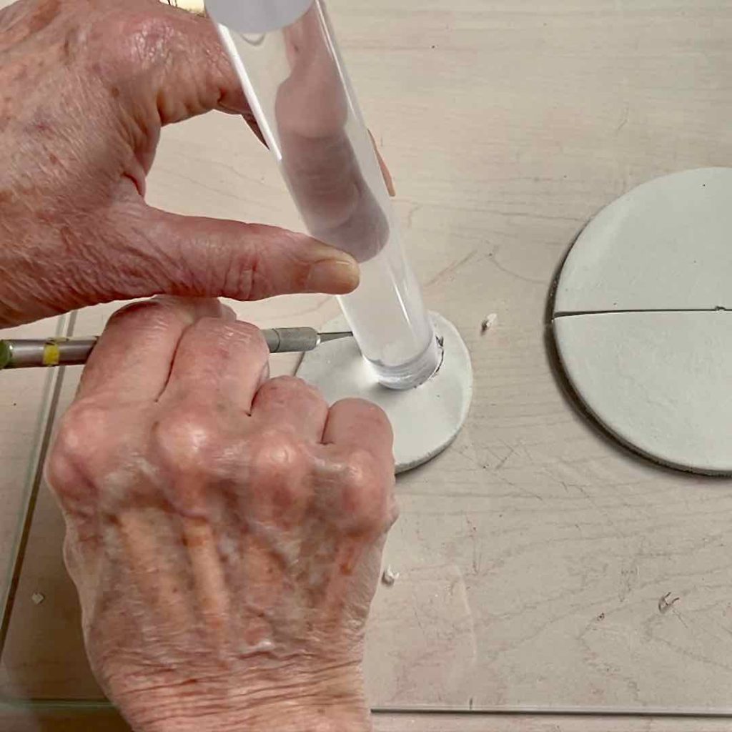 closeup of one hand holding an acrylic rod and the other cutting around it