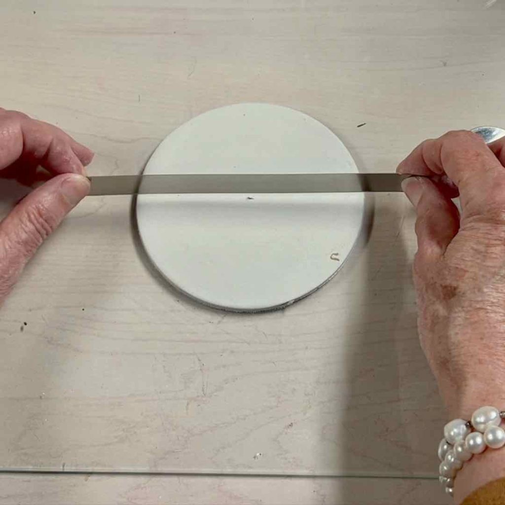 two hands holding a tissue blade across the center of the clay