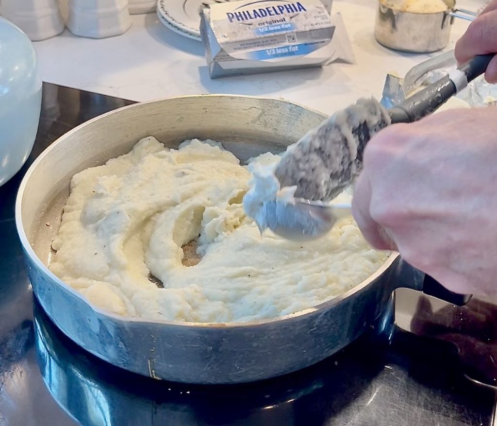 closeup of hand stirring Cauliflower Mash in a large skillet