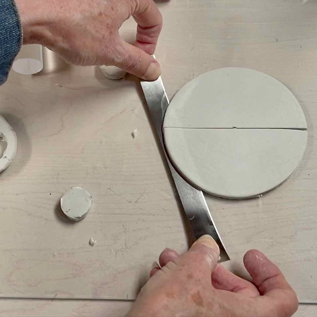 closeup of two hands using a tissue blade to lift the cut clay