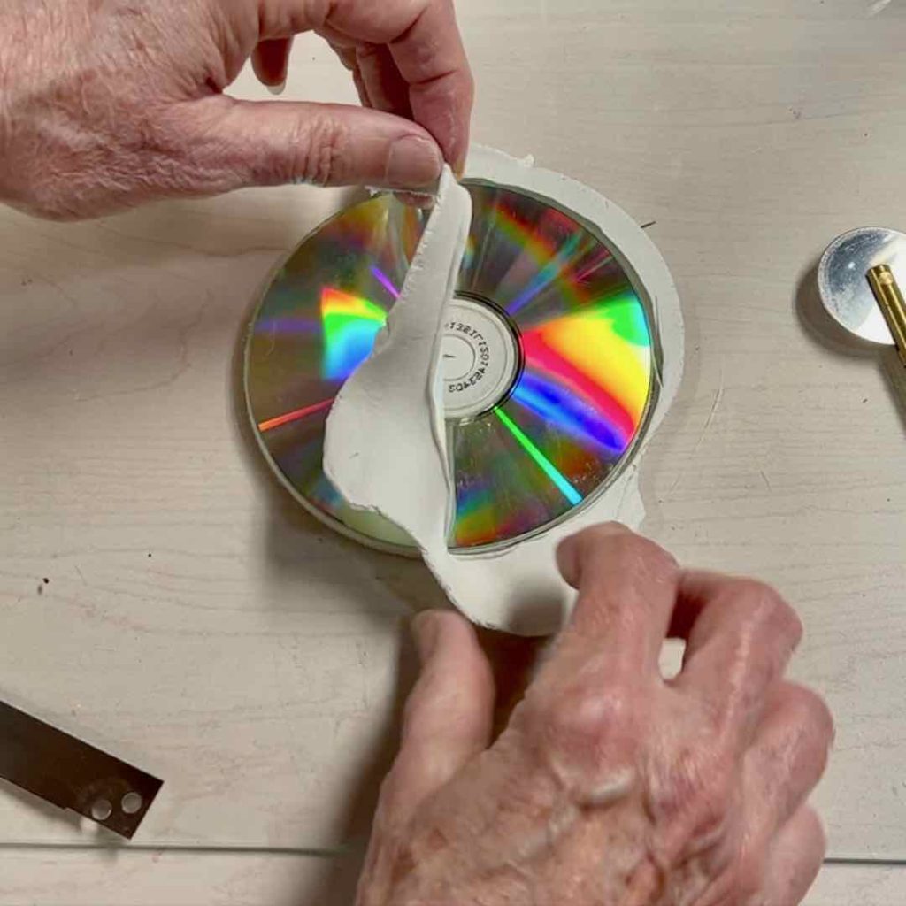 closeup of two hands removing the excess clay around the CD