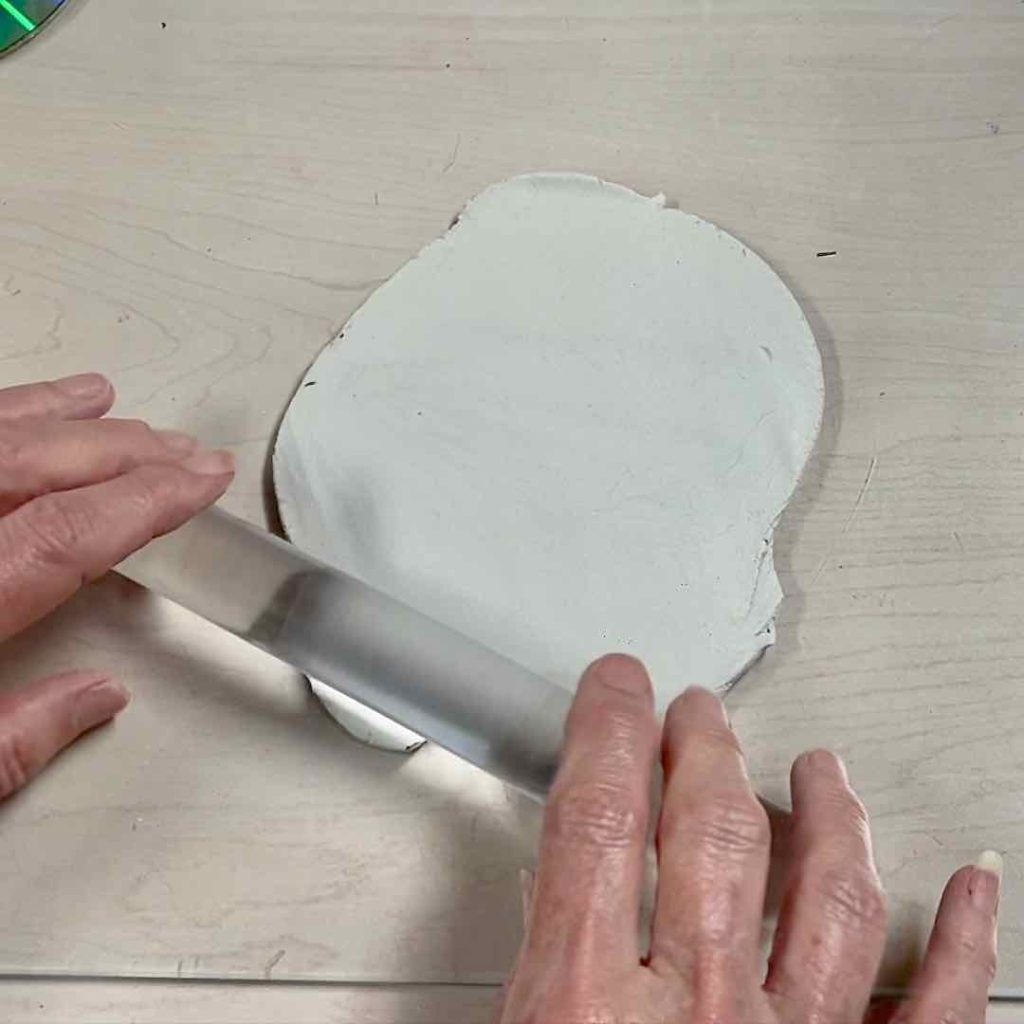 closeup of two hands rolling out the clay with an acrylic rod