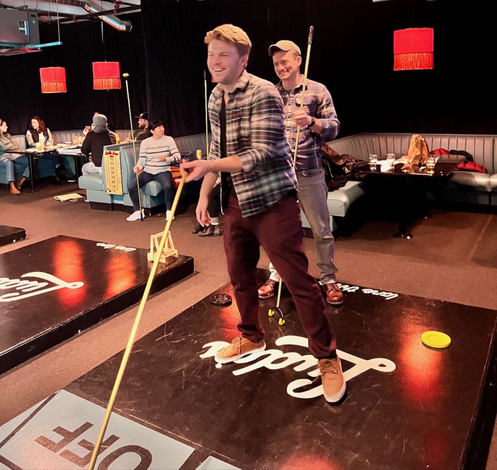 two young men playing shuffleboard in a bar