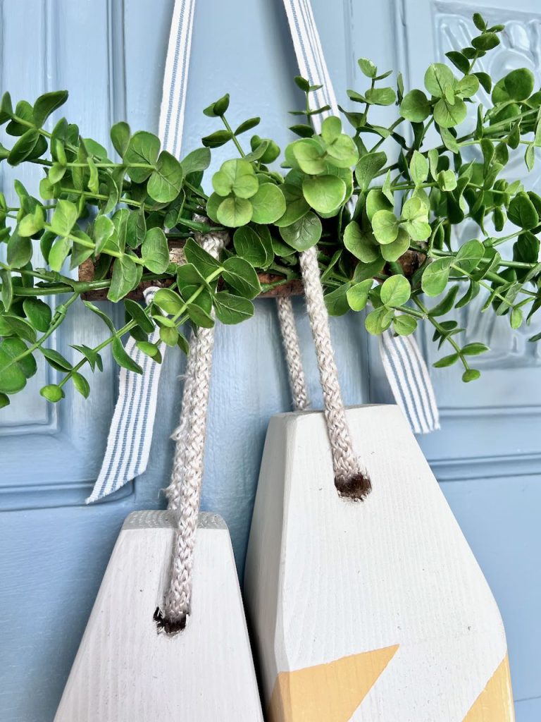 closeup of two wood buoys hanging on a stick with faux boxwood on a front door