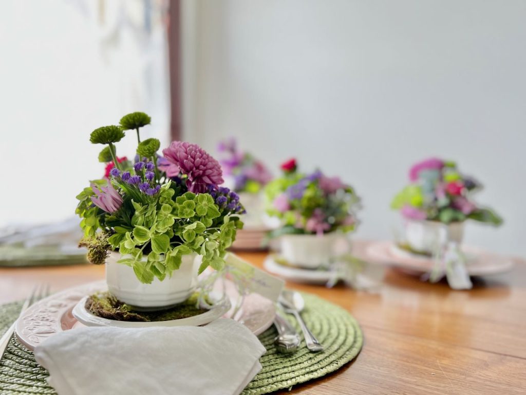 fresh flowers arranged in coffee cups on moss covered saucers