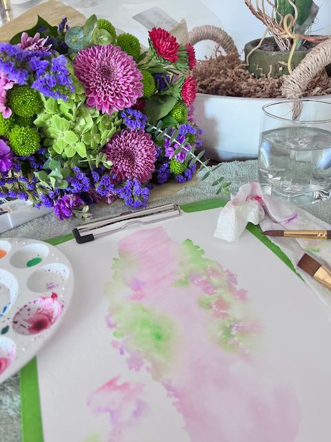 watercolor paper with palette and brushes next to a bundle of fresh flowers