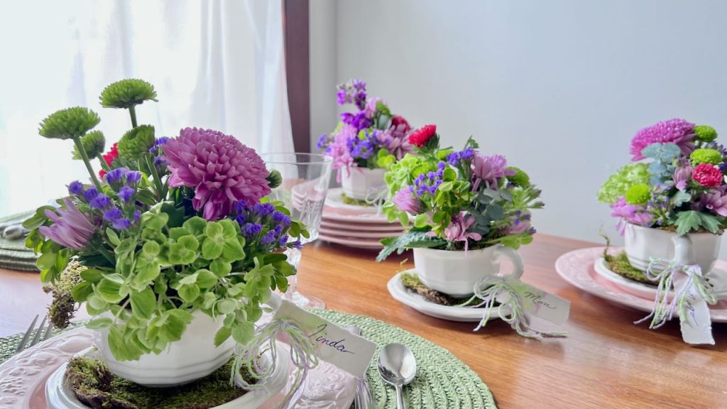 Close up of one cup and saucer filled with fresh flowers with two more cups in tthe background