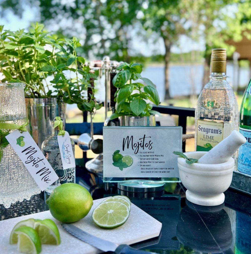 herbs in vintage cocktail shakers with a recipe for mojitos and bottles and limes on a bar cart