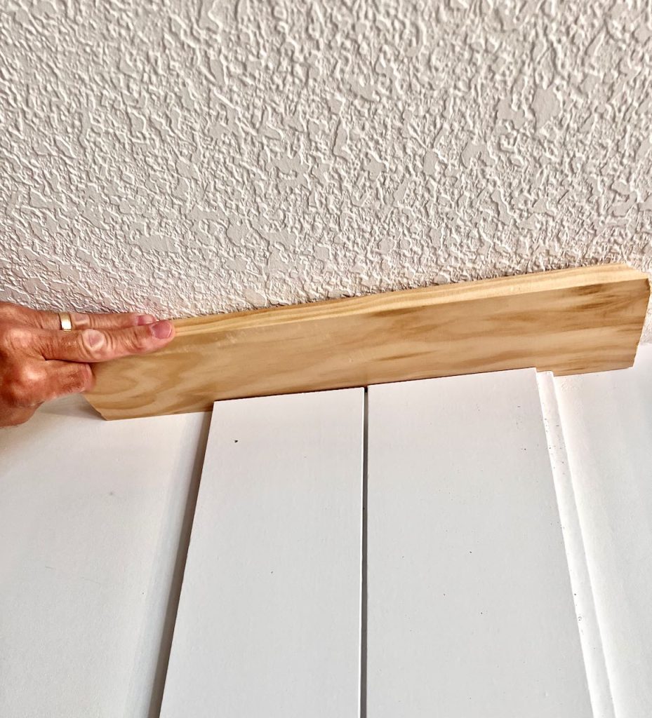 a man's hand holding a trim board between the ceiling and the shiplap backing.